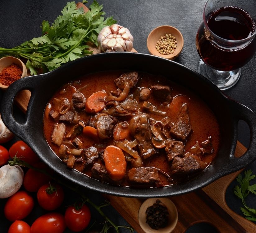 Boeuf bourgignon présenté dans une cassolette avec un verre de vin
