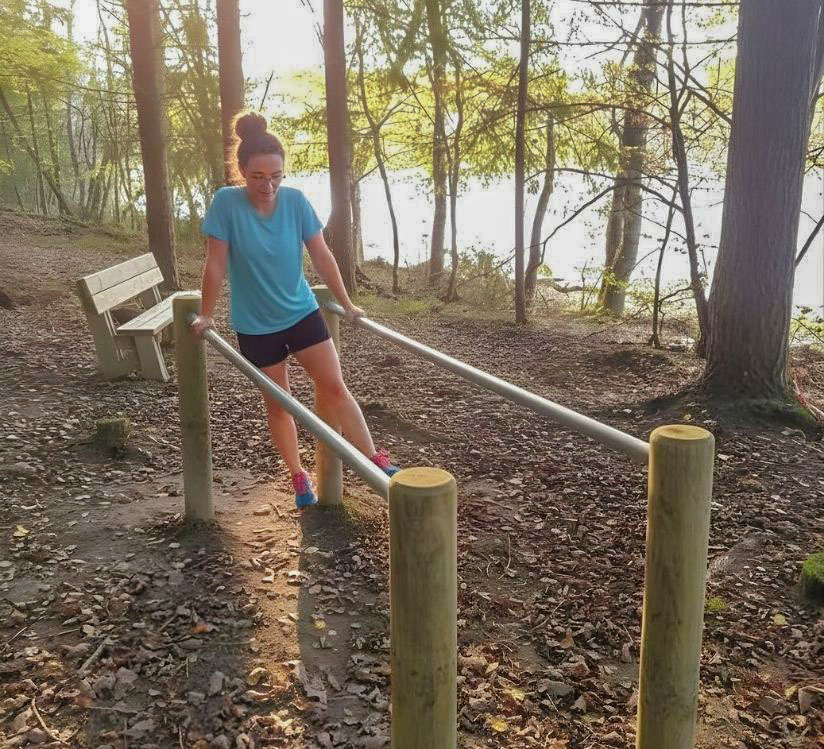 jeune femme qui fait des barres parellèles sur le parcours santé du camping en bord d'étange près de nevers