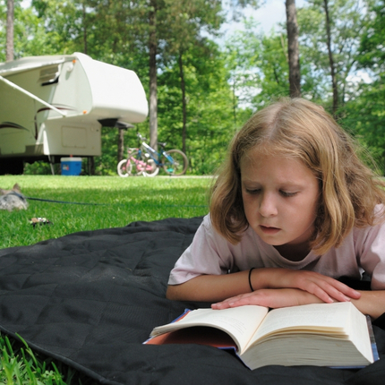 petite fille qui lit sur une couverture par terre au camping l'étang du merle